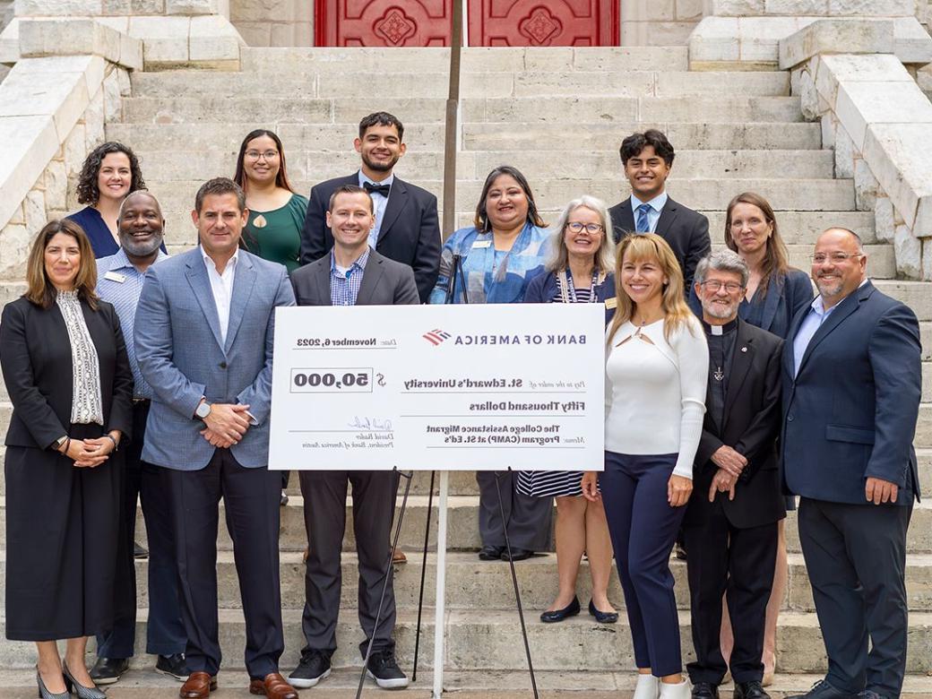 A group of business leaders, students and university administrators accept a check on the steps in front of Main Building.